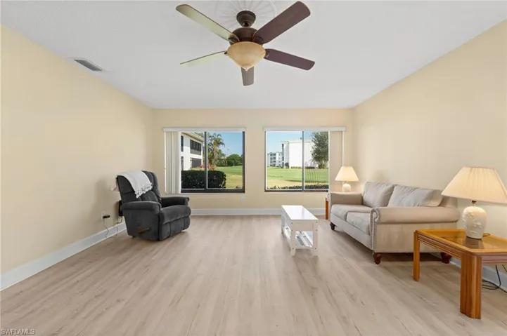 Spacious room featuring wood-finish flooring, two large windows, a ceiling fan, and baseboard molding