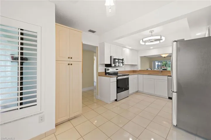 Kitchen featuring white cabinetry, stainless steel appliances, light-toned countertops, and tile flooring