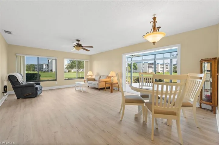 Open concept living and dining area featuring wood-finish flooring, multiple windows, a ceiling fan, and a decorative chandelier
