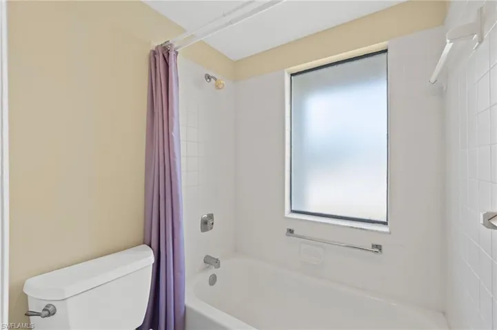 Bathtub with white subway tile surround, featuring a frosted window, chrome fixtures, and a shower curtain rod