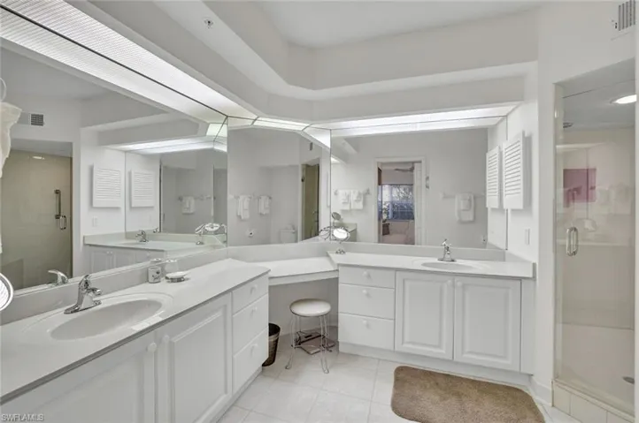 Bathroom featuring a stall shower, light tile patterned floors, and two vanities