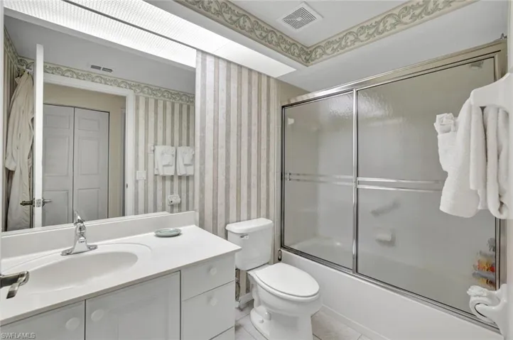 Bathroom featuring wallpapered walls, vanity, shower / bath combination with glass door, and light tile patterned floors