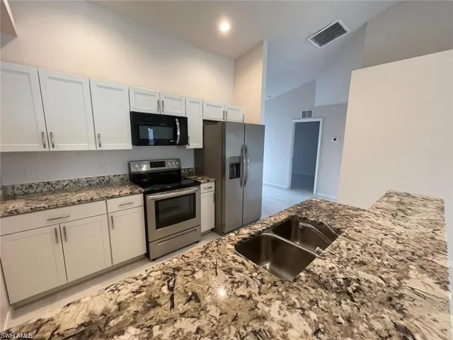 Kitchen with white cabinetry, stainless steel appliances, sink, and stone countertops