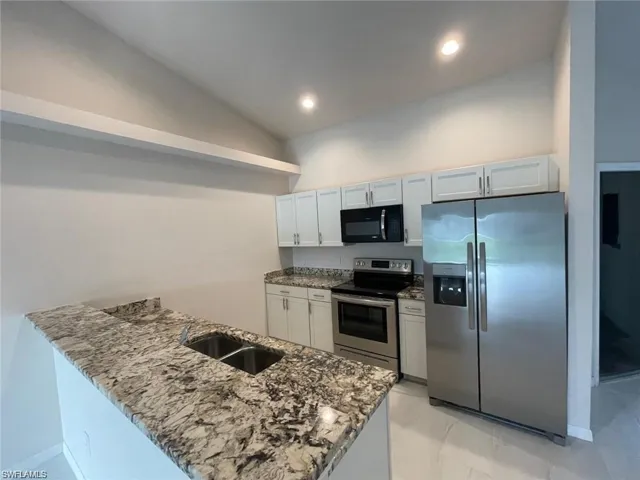Kitchen featuring light stone counters, stainless steel appliances, sink, vaulted ceiling, and white cabinets