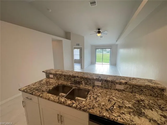 Kitchen with white cabinetry, sink, ceiling fan, dark stone countertops, and vaulted ceiling