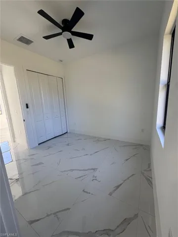 Unfurnished bedroom featuring a ceiling fan, light marble finish flooring, and a closet