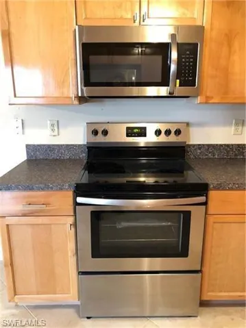 Kitchen with stainless steel appliances, dark countertops, and light tile patterned floors