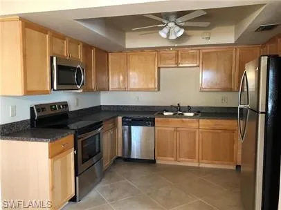 Kitchen featuring stainless steel appliances, a tray ceiling, dark countertops, and a ceiling fan