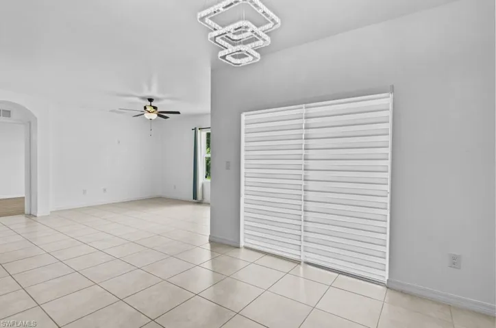 Tiled empty room featuring ceiling fan with notable chandelier