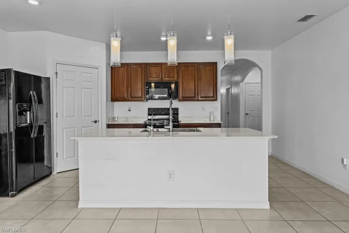Kitchen featuring black appliances, sink, decorative light fixtures, and a kitchen island with sink