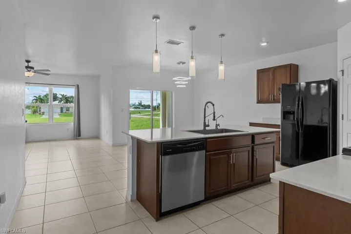 Kitchen with black fridge with ice dispenser, sink, ceiling fan, a kitchen island with sink, and stainless steel dishwasher