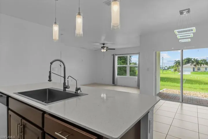 Kitchen with hanging light fixtures, light tile patterned floors, sink, ceiling fan, and a center island with sink
