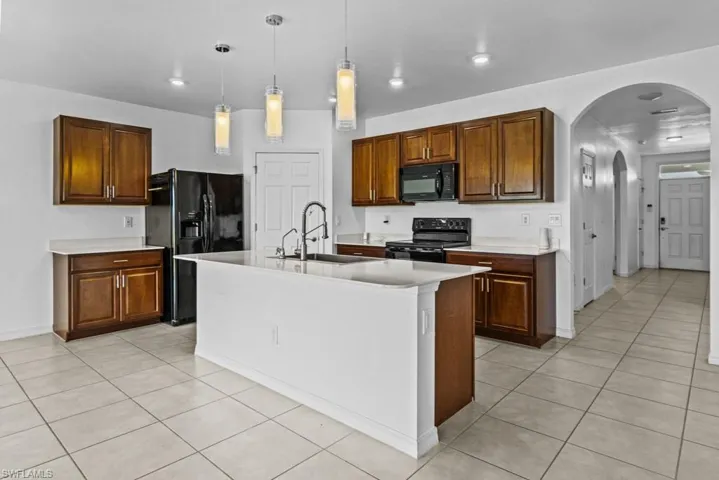 Kitchen featuring black appliances, light tile patterned floors, a kitchen island with sink, hanging light fixtures, and sink