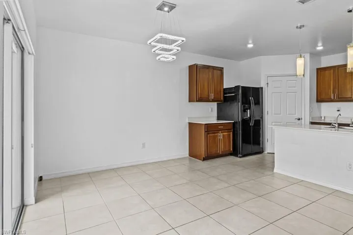 Kitchen with black fridge with ice dispenser, a chandelier, sink, hanging light fixtures, and light tile patterned flooring