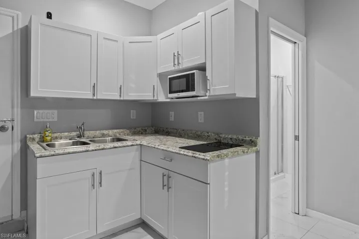 Kitchen with light stone counters, black electric cooktop, white cabinetry, and sink