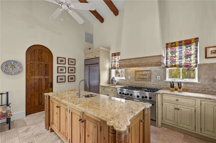 Kitchen with cream cabinets, high vaulted ceiling, premium appliances, a center island with sink, and beamed ceiling
