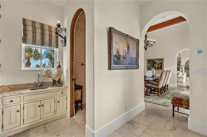 Hall with arched walkways, stone tile floors, a chandelier, and beamed ceiling