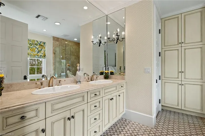Bathroom featuring wallpapered walls, ornamental molding, double vanity, a chandelier, and a shower stall