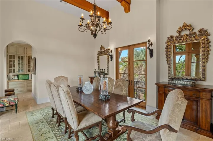 Dining area featuring a towering ceiling, beamed ceiling, arched walkways, stone tile flooring, and a chandelier