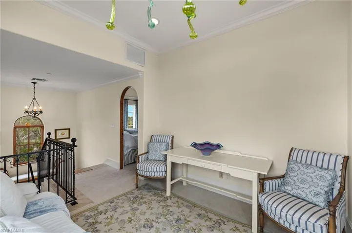 Living area with an upstairs landing, ornamental molding, carpet floors, arched walkways, and a chandelier