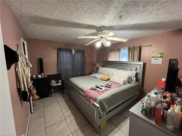Bedroom with light tile patterned floors, a ceiling fan, and a textured ceiling