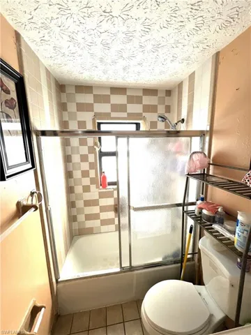 Bathroom with bath / shower combo with glass door, light tile patterned floors, and a textured ceiling