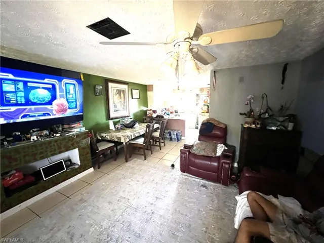 Living room with a textured ceiling, tile patterned floors, and ceiling fan
