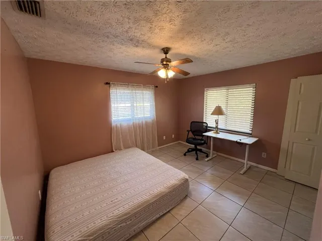 Bedroom with light tile patterned floors, ceiling fan, an office area, and a textured ceiling