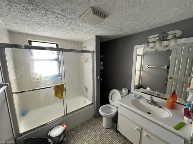Full bathroom featuring enclosed tub / shower combo, vanity, light tile patterned flooring, and a textured ceiling