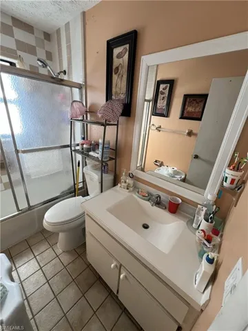 Full bathroom featuring vanity, a textured ceiling, bath / shower combo with glass door, and light tile patterned floors