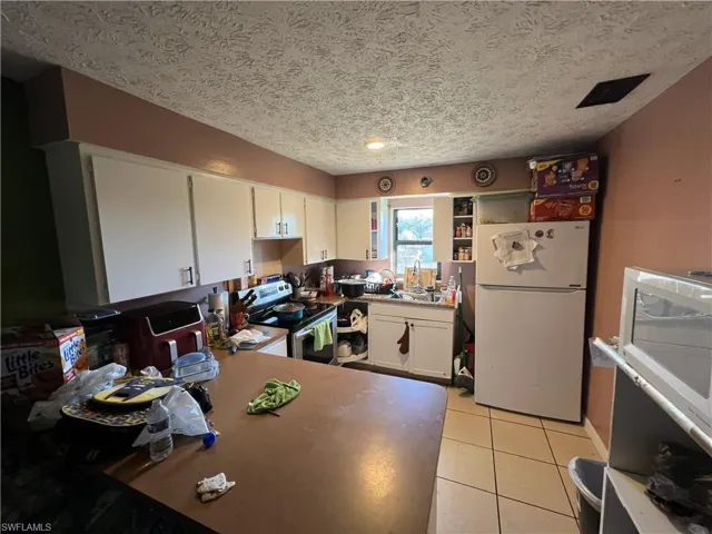 Kitchen with freestanding refrigerator, electric range, white cabinetry, light tile patterned flooring, and a textured ceiling