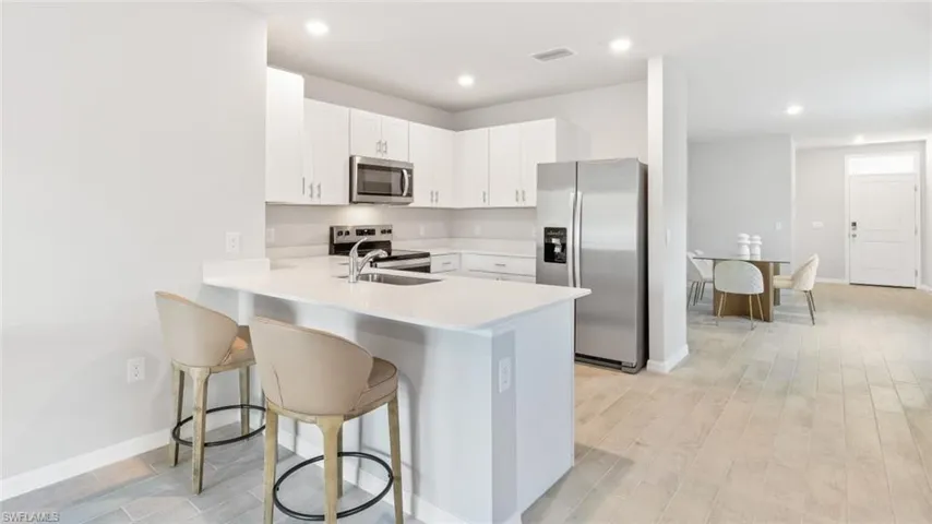 Kitchen featuring white cabinetry, a breakfast bar area, appliances with stainless steel finishes, light hardwood / wood-style flooring, and sink