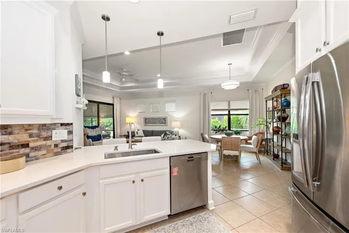 Kitchen featuring a tray ceiling, white cabinets, appliances with stainless steel finishes, ornamental molding, and open floor plan