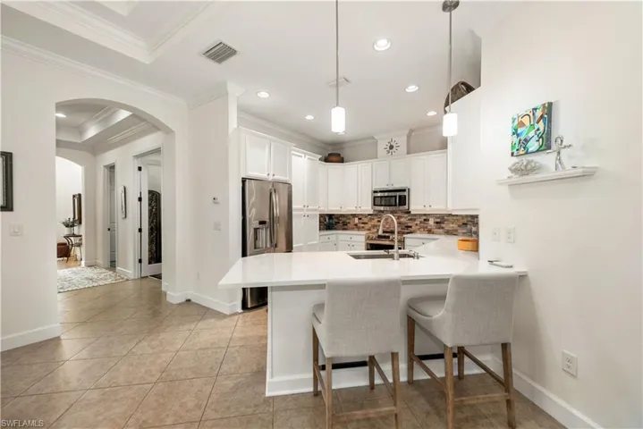 Kitchen featuring arched walkways, a kitchen bar, backsplash, appliances with stainless steel finishes, and white cabinets