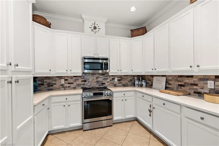 Kitchen with backsplash, appliances with stainless steel finishes, white cabinets, ornamental molding, and recessed lighting