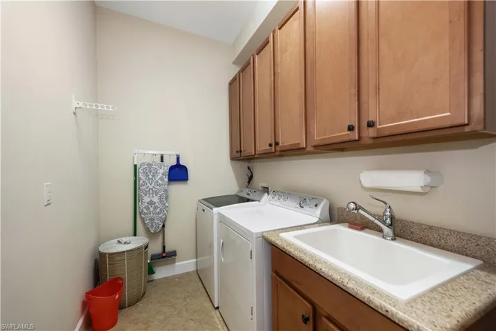 Laundry room with washer and dryer, light tile floors, wash sink and cabinet space