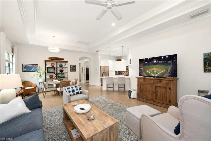 Living area with arched walkways, a tray ceiling, crown molding, light tile floors, and recessed lighting