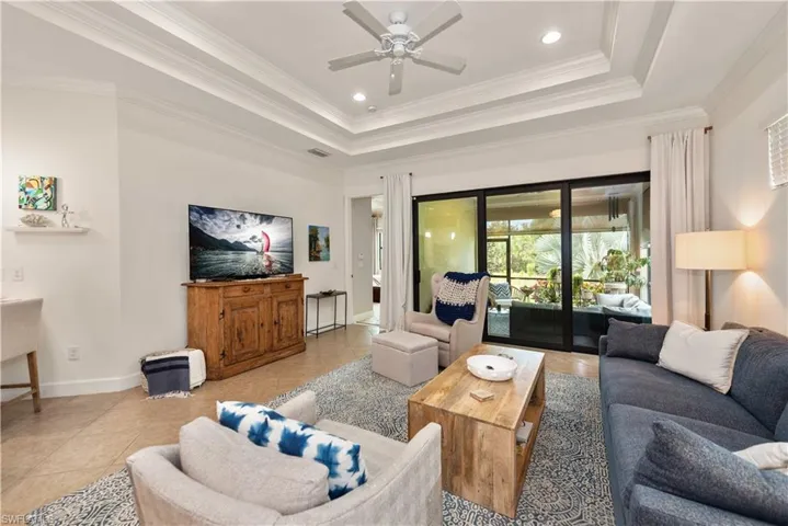 Tiled living room with a tray ceiling, crown molding, recessed lighting, and ceiling fan