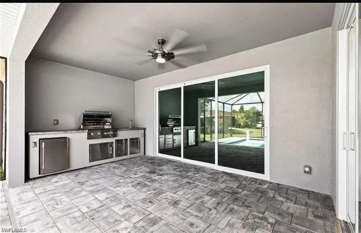 View of patio with an outdoor kitchen, a ceiling fan, and glass enclosure