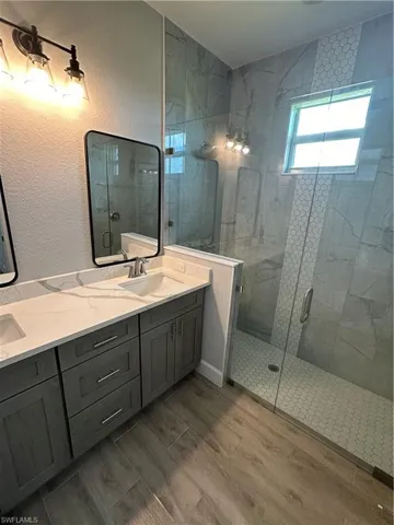 Full bathroom featuring a stall shower, a textured wall, double vanity, and wood tiled floors