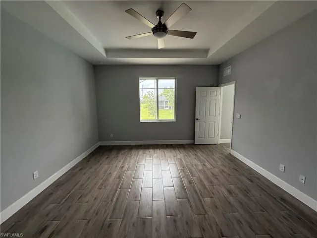 Empty room featuring wood finish floors, a raised ceiling, and ceiling fan