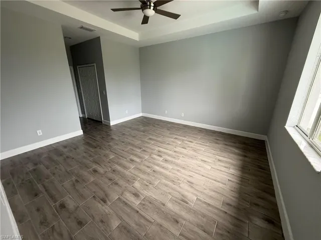 Empty room with a raised ceiling, ceiling fan, and wood tiled floors