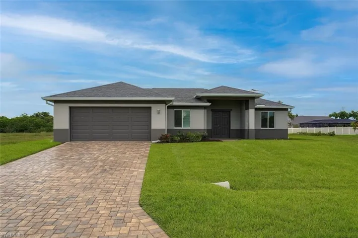 View of front facade with stucco siding, decorative driveway, a shingled roof, and an attached garage