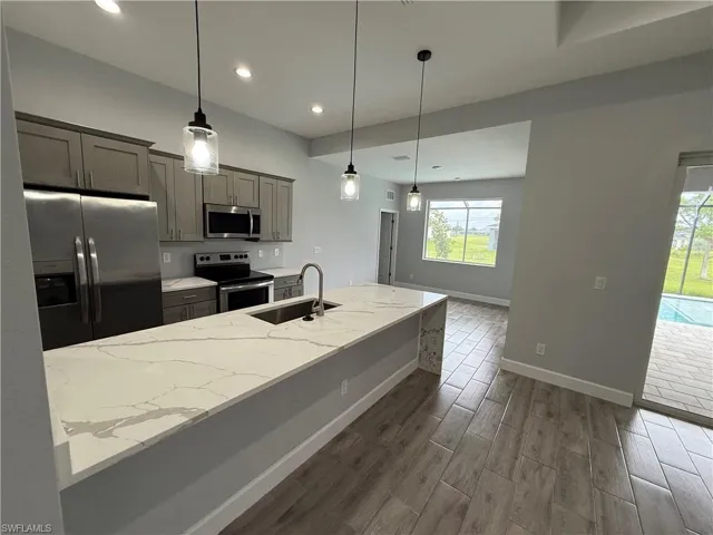 Kitchen with stainless steel appliances, wood finish floors, light stone countertops, pendant lighting, and gray cabinetry
