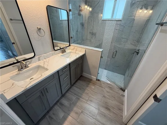 Bathroom with double vanity, plenty of natural light, a marble finish shower, a textured wall, and wood finish floors