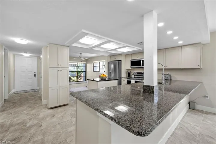 Kitchen featuring dark stone counters, ceiling fan, kitchen peninsula, stainless steel appliances, and light tile flooring