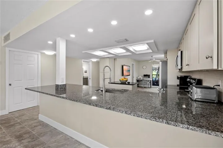 Kitchen featuring dark stone counters, ceiling fan, kitchen peninsula, light tile floors, and sink