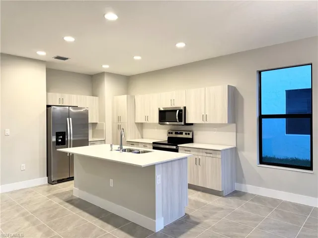 Kitchen featuring stainless steel appliances, light tile patterned flooring, sink, and a kitchen island with sink