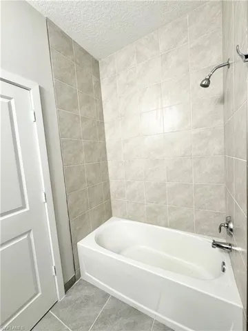 Bathroom with tile patterned flooring, tiled shower / bath combo, and a textured ceiling