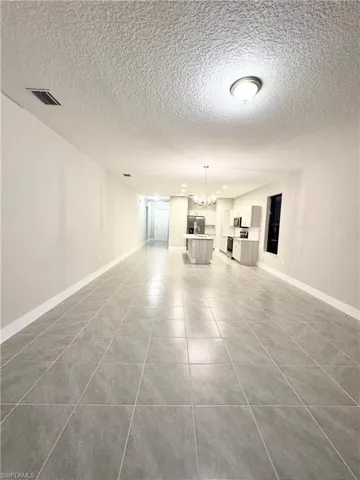 Unfurnished living room featuring tile patterned floors, a textured ceiling, and a notable chandelier